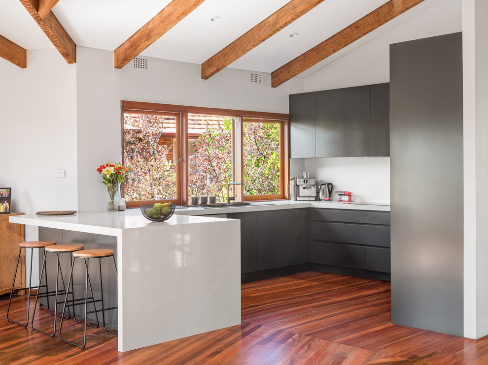 Inspiration for a mid-sized contemporary u-shaped open plan kitchen in Sydney with a double-bowl sink, recessed-panel cabinets, black cabinets, quartz benchtops, white splashback, glass sheet splashback, stainless steel appliances, medium hardwood floors, no island, brown floor and white benchtop.