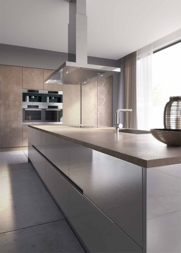 Photo of an expansive modern single-wall open plan kitchen in London with an integrated sink, flat-panel cabinets, beige cabinets, concrete benchtops, beige splashback, panelled appliances, porcelain floors and with island.