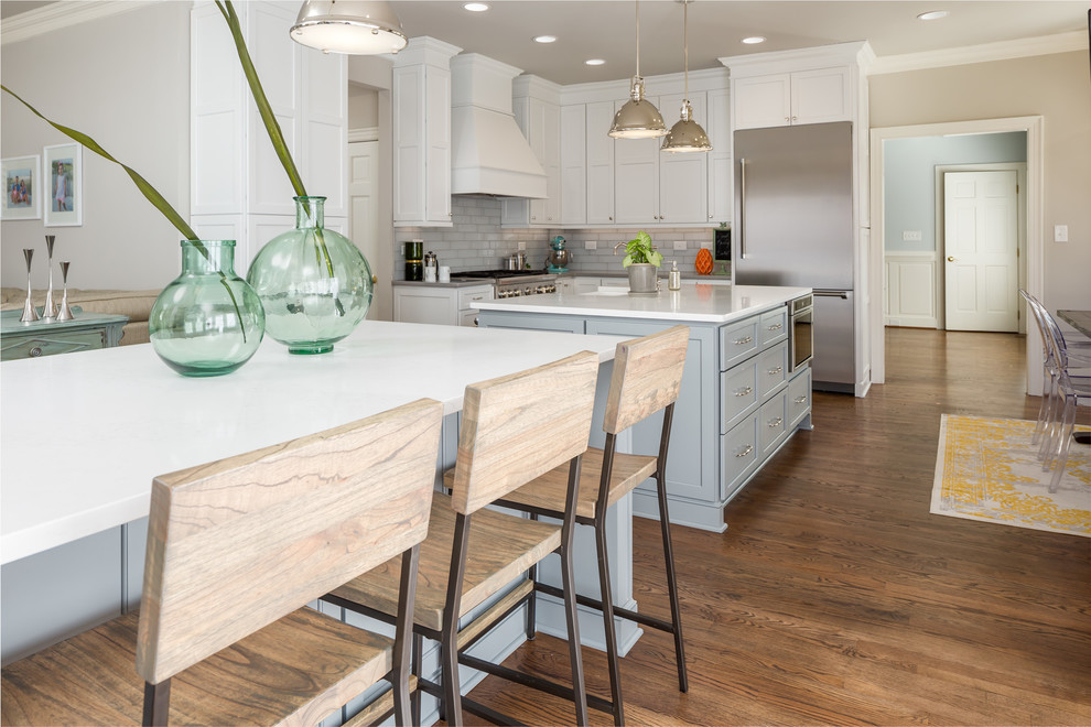 Photo of an expansive transitional galley open plan kitchen in Raleigh with a farmhouse sink, flat-panel cabinets, white cabinets, quartz benchtops, grey splashback, ceramic splashback, stainless steel appliances, medium hardwood floors and multiple islands.