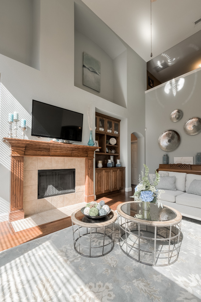 Inspiration for a large transitional open concept family room in Dallas with grey walls, medium hardwood floors, a standard fireplace, a tile fireplace surround and a wall-mounted tv.