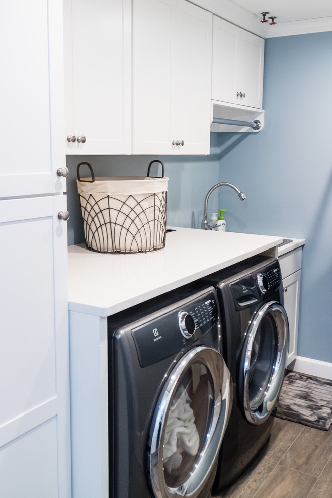 Mid-sized transitional single-wall porcelain tile and brown floor dedicated laundry room photo in New York with an undermount sink, shaker cabinets, white cabinets, quartz countertops, blue walls and a side-by-side washer/dryer