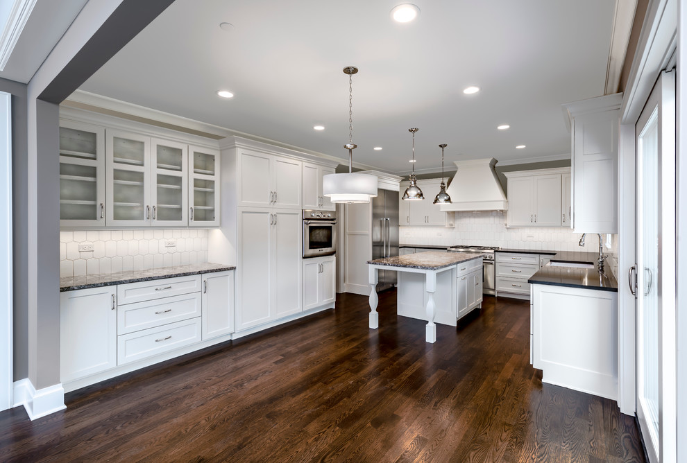 Inspiration for a mid-sized transitional u-shaped separate kitchen in Chicago with an undermount sink, shaker cabinets, white cabinets, granite benchtops, white splashback, ceramic splashback, stainless steel appliances, dark hardwood floors, with island and brown floor.
