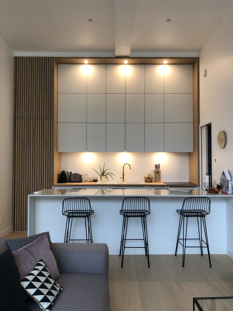 Photo of a scandinavian open plan kitchen in Paris with flat-panel cabinets, grey cabinets, white splashback, a peninsula, light hardwood floors, beige floor and grey benchtop.