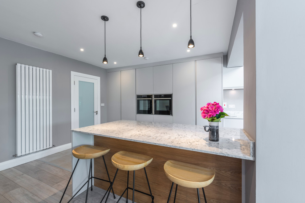 Inspiration for a mid-sized contemporary galley open plan kitchen in Dublin with a drop-in sink, grey cabinets, quartzite benchtops, engineered quartz splashback, panelled appliances, porcelain floors, a peninsula, grey floor, flat-panel cabinets, blue splashback and blue benchtop.