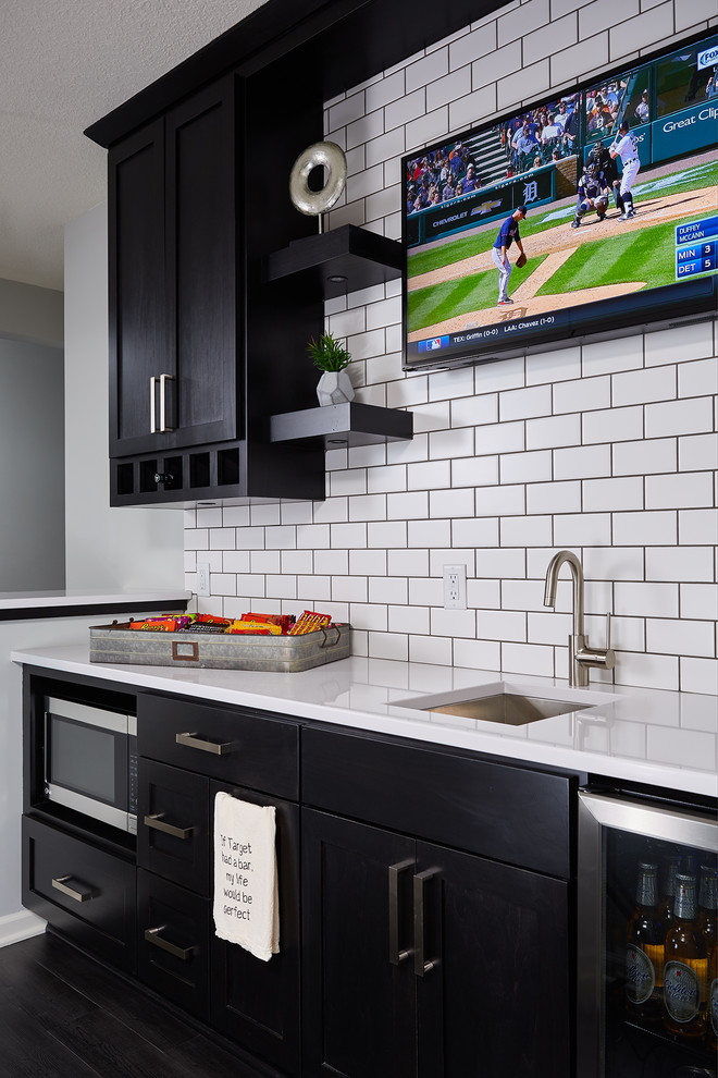 Design ideas for a small industrial l-shaped wet bar in Minneapolis with an undermount sink, recessed-panel cabinets, black cabinets, quartzite benchtops, white splashback, subway tile splashback, dark hardwood floors and brown floor.