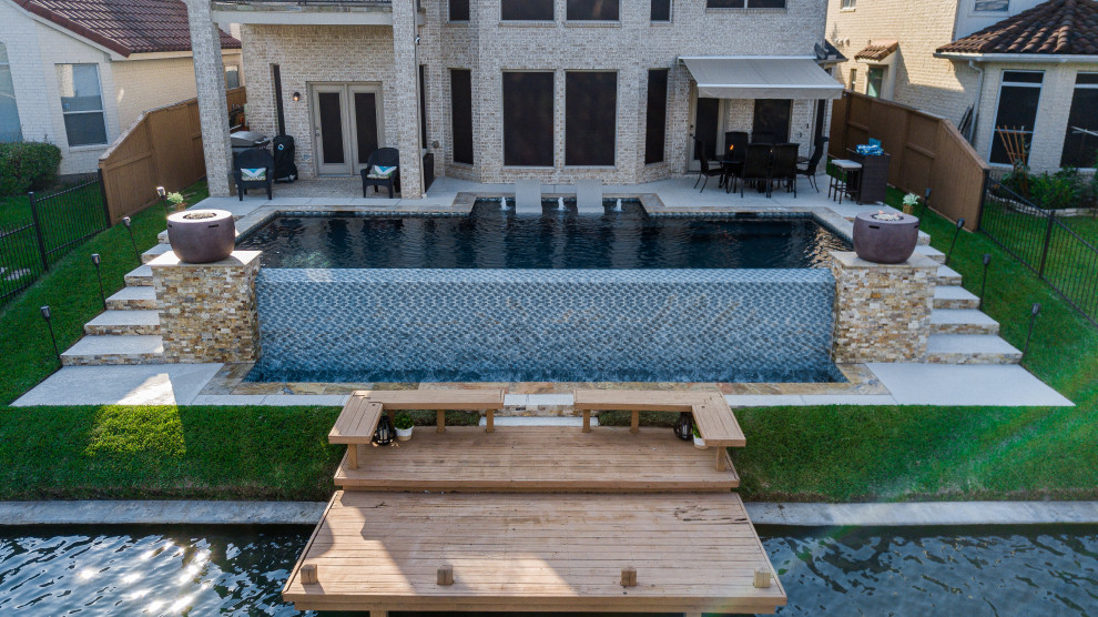 Идея дизайна: большой прямоугольный бассейн-инфинити на заднем дворе в современном стиле с настилом