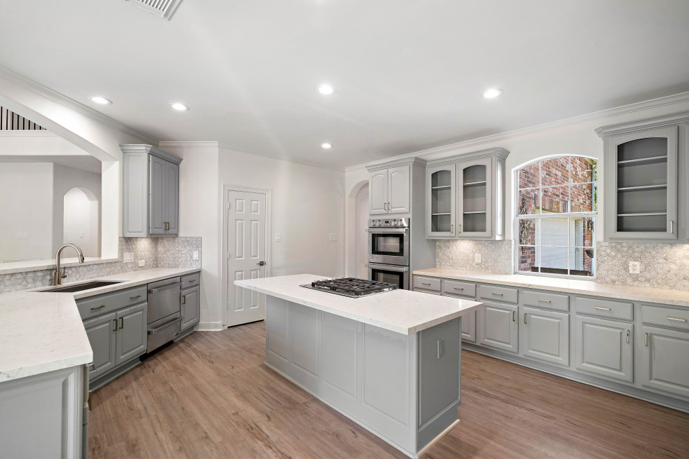 Mid-sized transitional u-shaped light wood floor and brown floor eat-in kitchen photo in Houston with raised-panel cabinets, gray cabinets, white backsplash, marble backsplash, stainless steel appliances, an island, white countertops, quartz countertops and an undermount sink