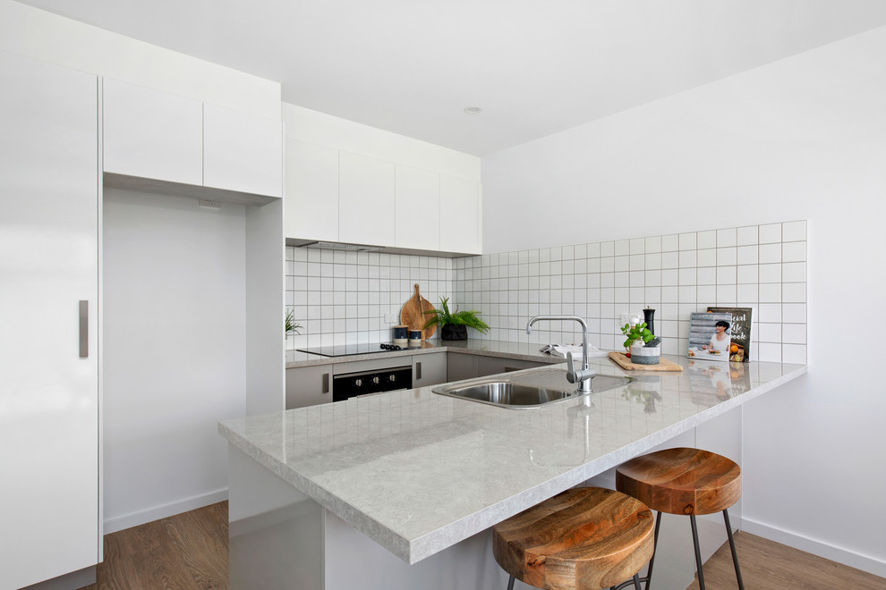 Small u-shaped open plan kitchen in Other with a drop-in sink, grey cabinets, laminate benchtops, white splashback, ceramic splashback, black appliances, vinyl floors, no island, brown floor and grey benchtop.
