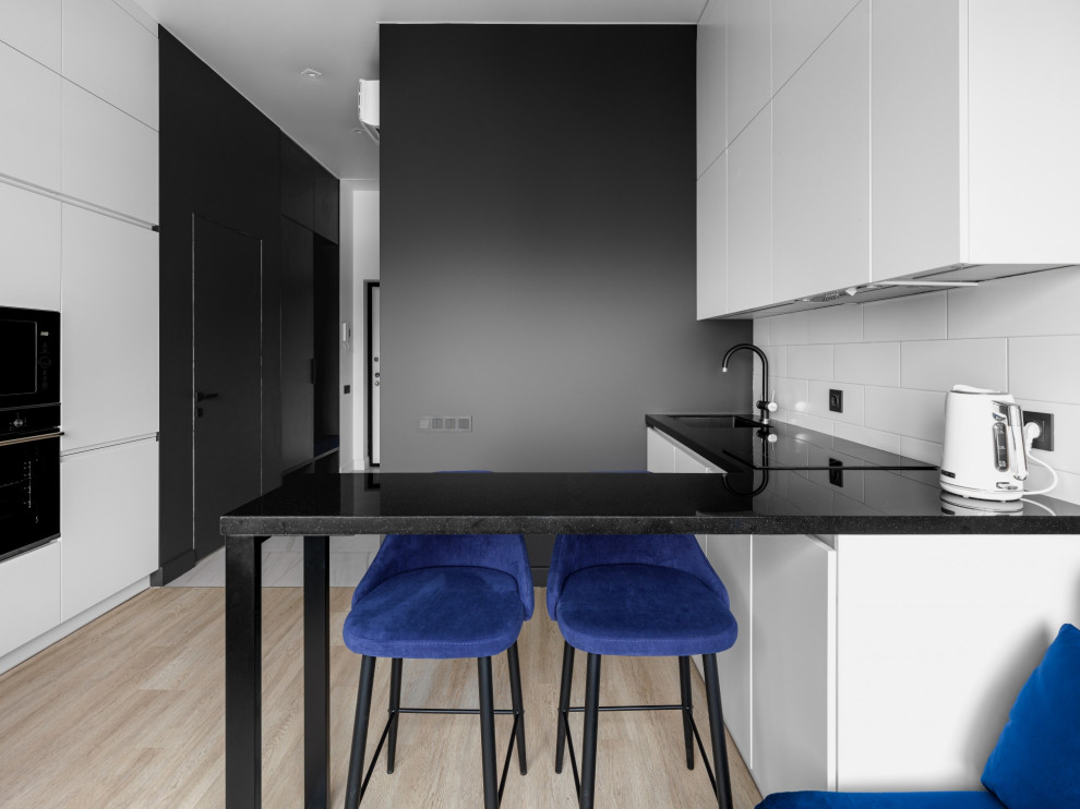 Small contemporary galley open plan kitchen in Other with a submerged sink, flat-panel cabinets, white cabinets, engineered stone countertops, white splashback, black appliances, laminate floors, no island, beige floors and black worktops.