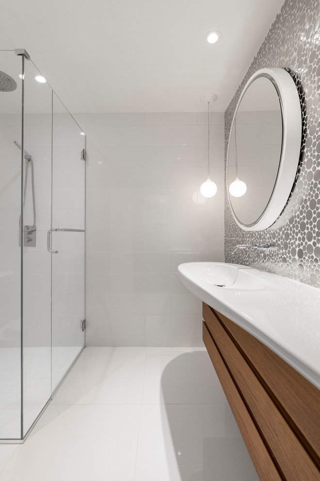 Photo of a small contemporary kids bathroom with flat-panel cabinets, medium wood cabinets, a curbless shower, a one-piece toilet, white tile, metal tile, ceramic floors, a wall-mount sink, solid surface benchtops, white floor and a hinged shower door.