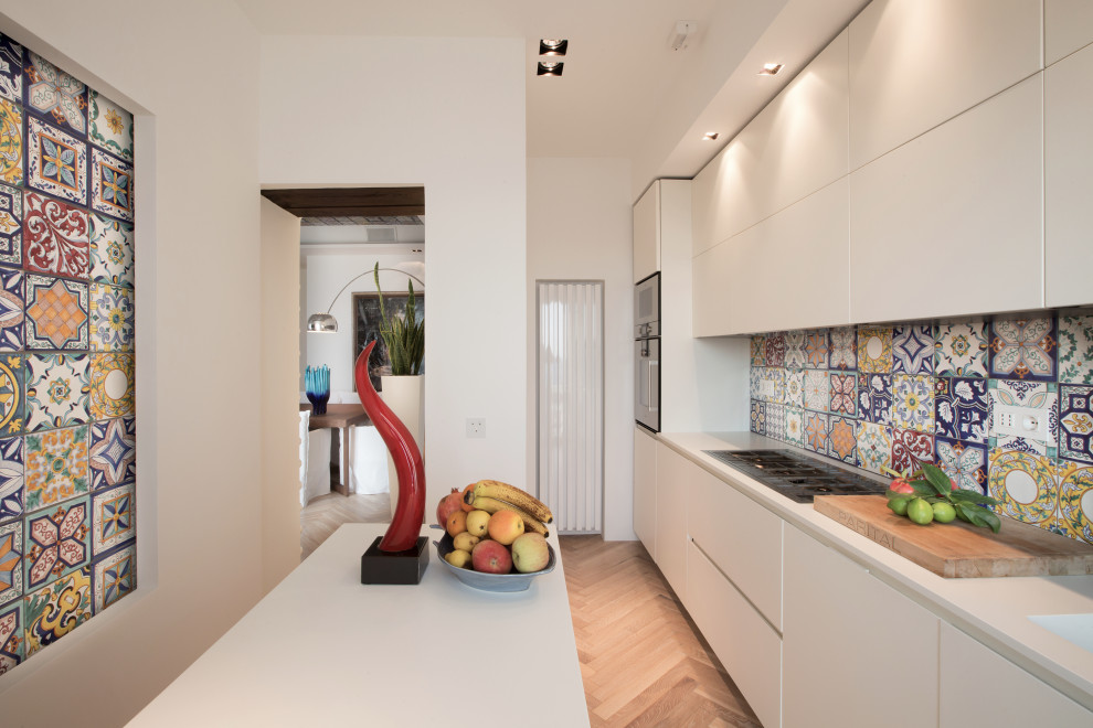 This is an example of a small mediterranean single-wall separate kitchen in Other with an integrated sink, flat-panel cabinets, white cabinets, solid surface benchtops, multi-coloured splashback, ceramic splashback, stainless steel appliances, light hardwood floors, with island, yellow floor and white benchtop.