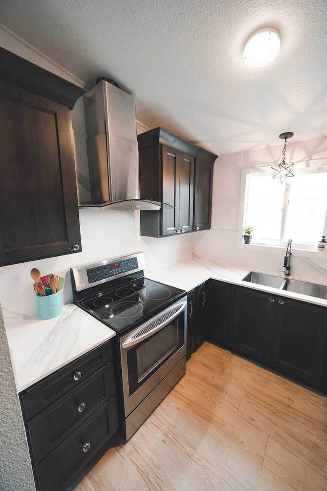 This is an example of a small transitional u-shaped separate kitchen in Seattle with an undermount sink, recessed-panel cabinets, dark wood cabinets, quartz benchtops, white splashback, stone slab splashback, stainless steel appliances, vinyl floors, no island, brown floor and white benchtop.
