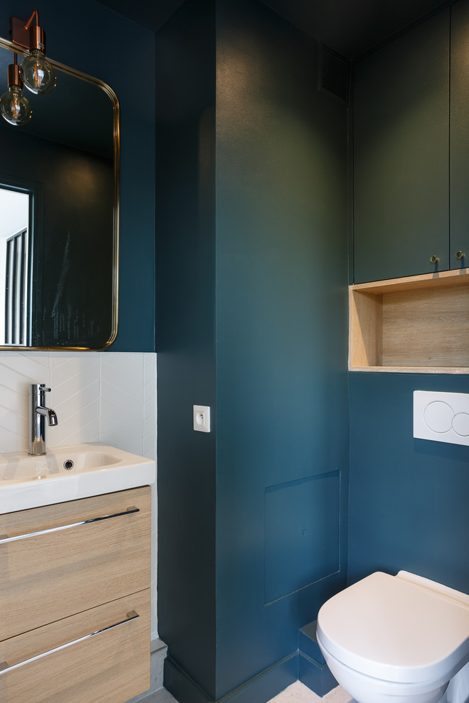 This is an example of a mid-sized scandinavian master bathroom in Other with flat-panel cabinets, light wood cabinets, an alcove shower, a wall-mount toilet, white tile, porcelain tile, blue walls, terrazzo floors, a wall-mount sink, solid surface benchtops, grey floor, a sliding shower screen and white benchtops.