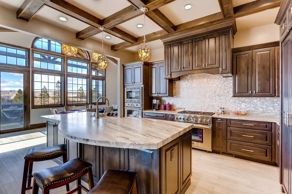 Large transitional u-shaped eat-in kitchen in Denver with a farmhouse sink, raised-panel cabinets, dark wood cabinets, limestone benchtops, metallic splashback, mosaic tile splashback, stainless steel appliances, porcelain floors, with island, beige floor and beige benchtop.