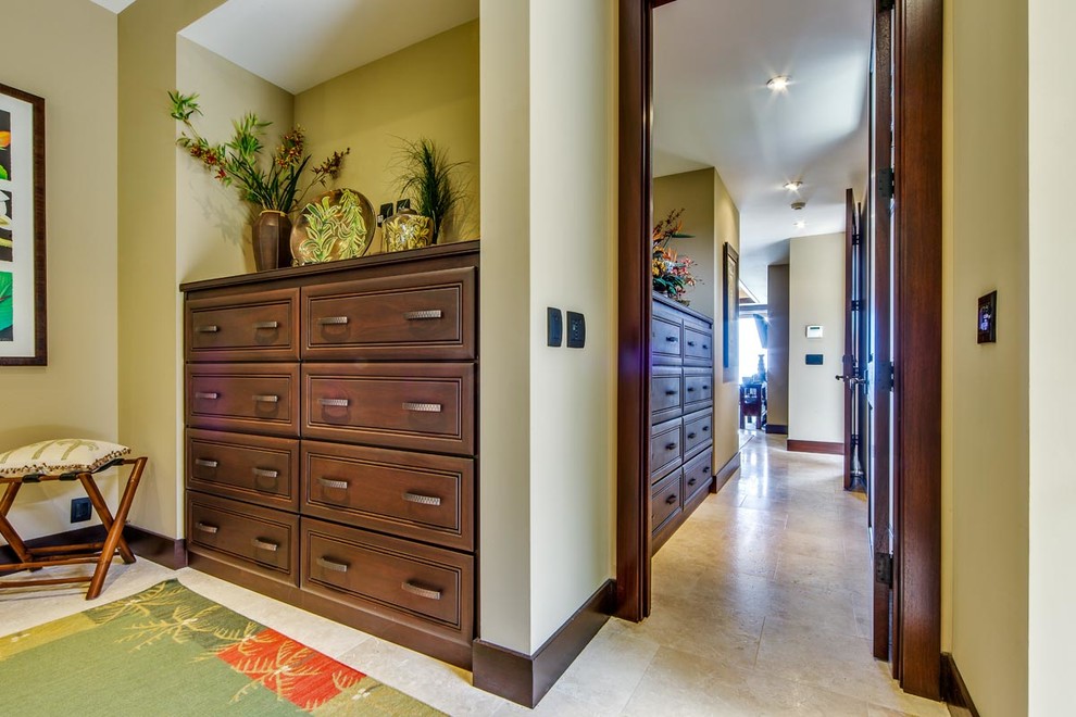 Mid-sized tropical gender-neutral dressing room in Hawaii with raised-panel cabinets, brown cabinets and travertine floors.