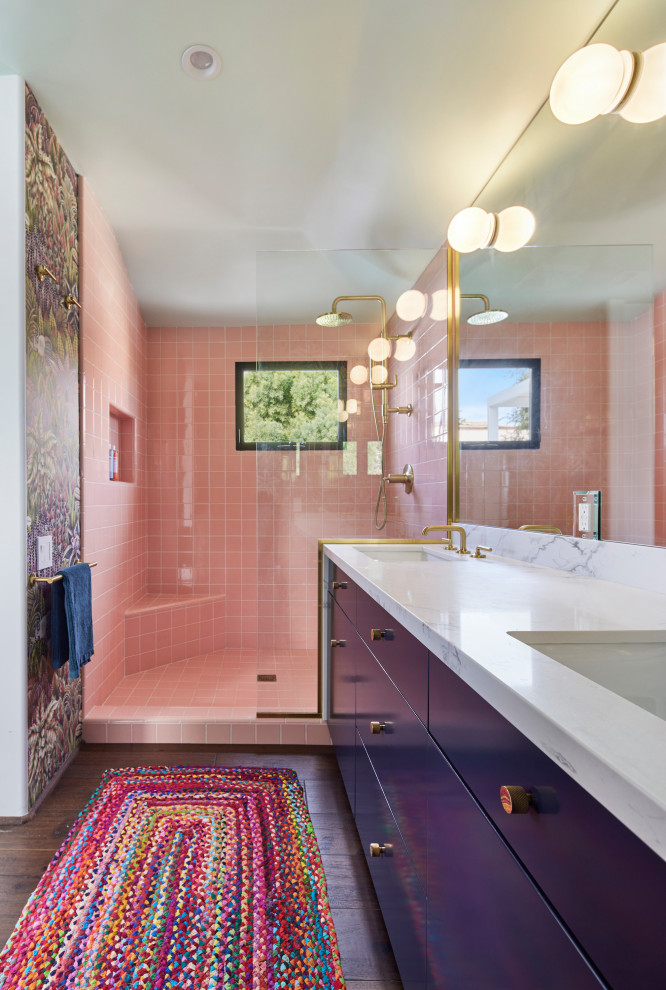 Photo of a medium sized mediterranean ensuite bathroom in Los Angeles with flat-panel cabinets, blue cabinets, a walk-in shower, a one-piece toilet, pink tiles, ceramic tiles, multi-coloured walls, dark hardwood flooring, a submerged sink, engineered stone worktops, brown floors, an open shower, white worktops, an enclosed toilet, double sinks, a built in vanity unit and wallpapered walls.