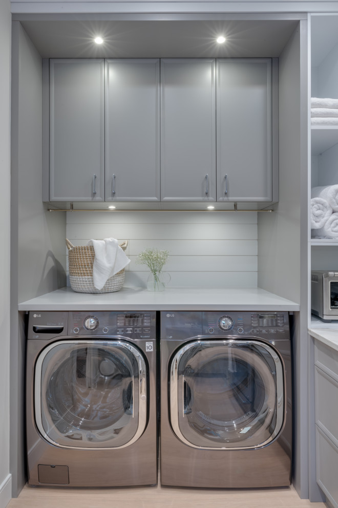 Photo of a small contemporary single-wall utility room in Vancouver with flat-panel cabinets, grey cabinets, grey splashback, light hardwood floors, a side-by-side washer and dryer, beige floor, white benchtop and planked wall panelling.