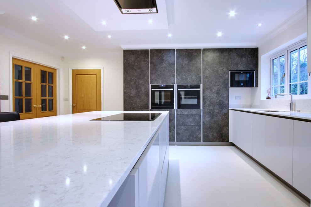 Photo of a mid-sized contemporary u-shaped eat-in kitchen in Hertfordshire with an undermount sink, flat-panel cabinets, white cabinets, quartzite benchtops, white splashback, stone slab splashback, black appliances and with island.