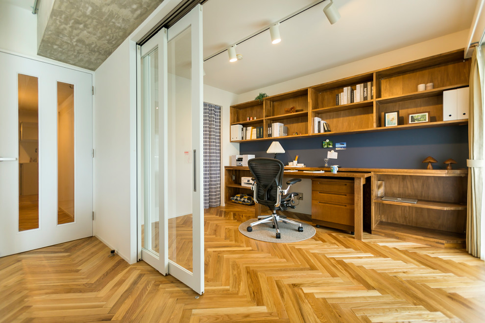 This is an example of a scandinavian home office in Other with white walls, medium hardwood floors, a built-in desk and brown floor.