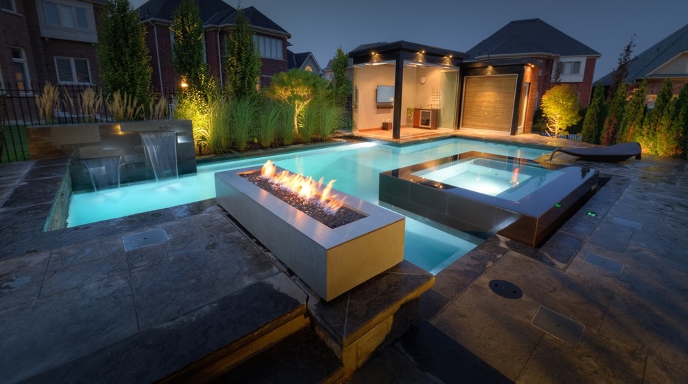 Design ideas for a mid-sized contemporary backyard custom-shaped lap pool in Toronto with a hot tub and natural stone pavers.