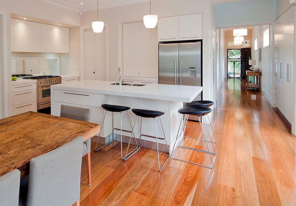 Inspiration for a large contemporary l-shaped eat-in kitchen in Melbourne with an undermount sink, flat-panel cabinets, white cabinets, stainless steel appliances, quartz benchtops, metallic splashback, with island, glass tile splashback and medium hardwood floors.