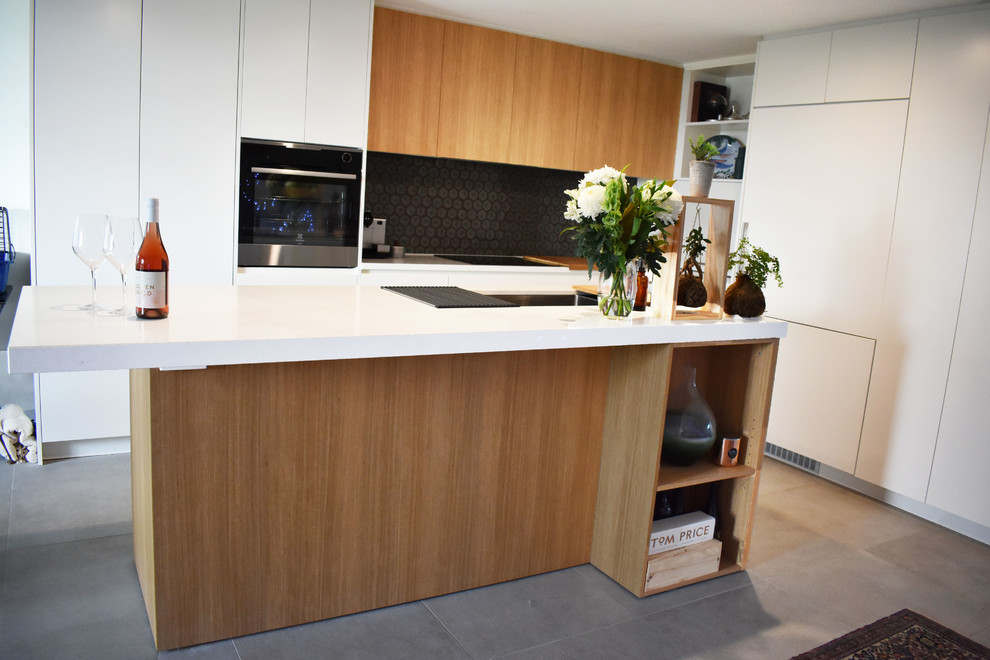 This is an example of a mid-sized contemporary l-shaped kitchen in Adelaide with an undermount sink, flat-panel cabinets, white cabinets, quartz benchtops, black splashback, mosaic tile splashback, ceramic floors, with island and grey floor.