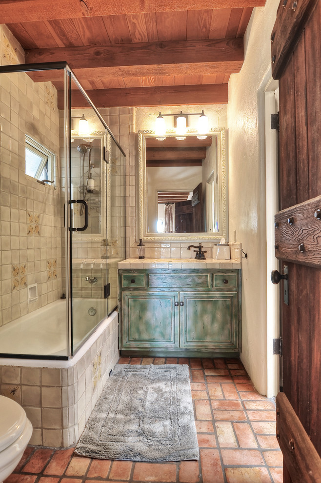 Expansive mediterranean master bathroom in Orange County with beaded inset cabinets, distressed cabinets, a corner shower, white tile, ceramic tile, white walls, an integrated sink, tile benchtops, a drop-in tub, terra-cotta floors and a hinged shower door.