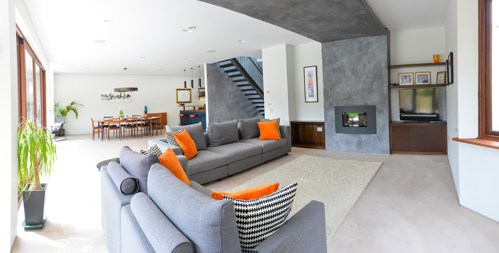 Large contemporary open concept living room in Sussex with grey walls, concrete floors, a standard fireplace, a plaster fireplace surround and a built-in media wall.
