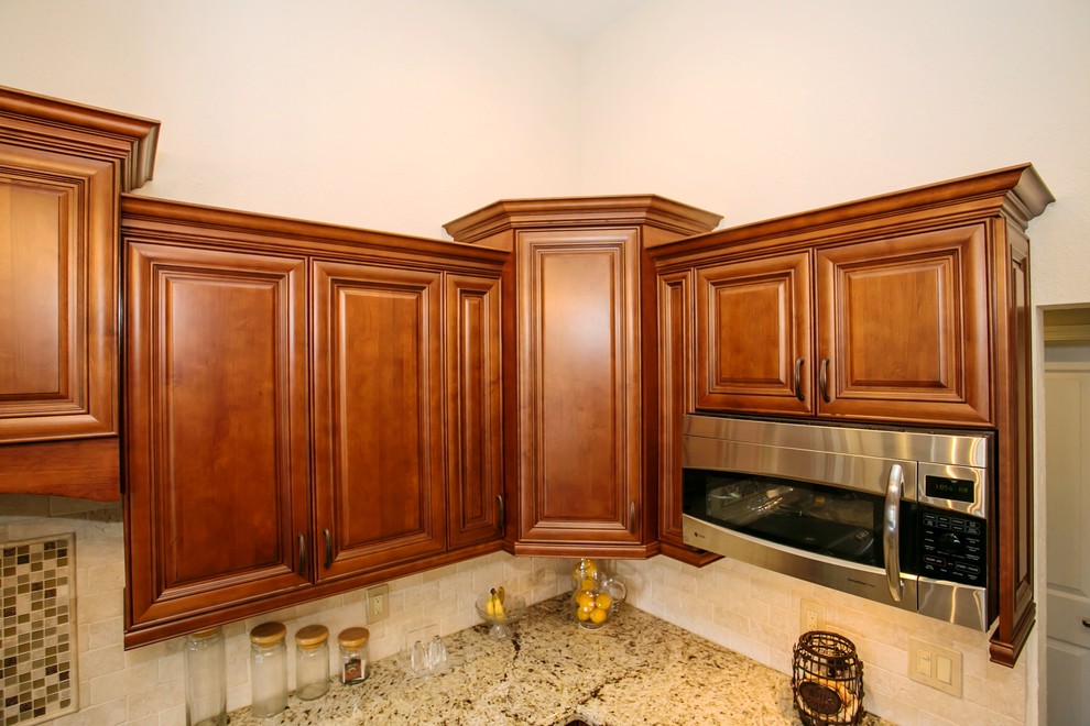 Inspiration for a mid-sized transitional u-shaped porcelain tile eat-in kitchen remodel in Miami with an undermount sink, raised-panel cabinets, brown cabinets, granite countertops, beige backsplash, stone tile backsplash, stainless steel appliances, beige walls and a peninsula
