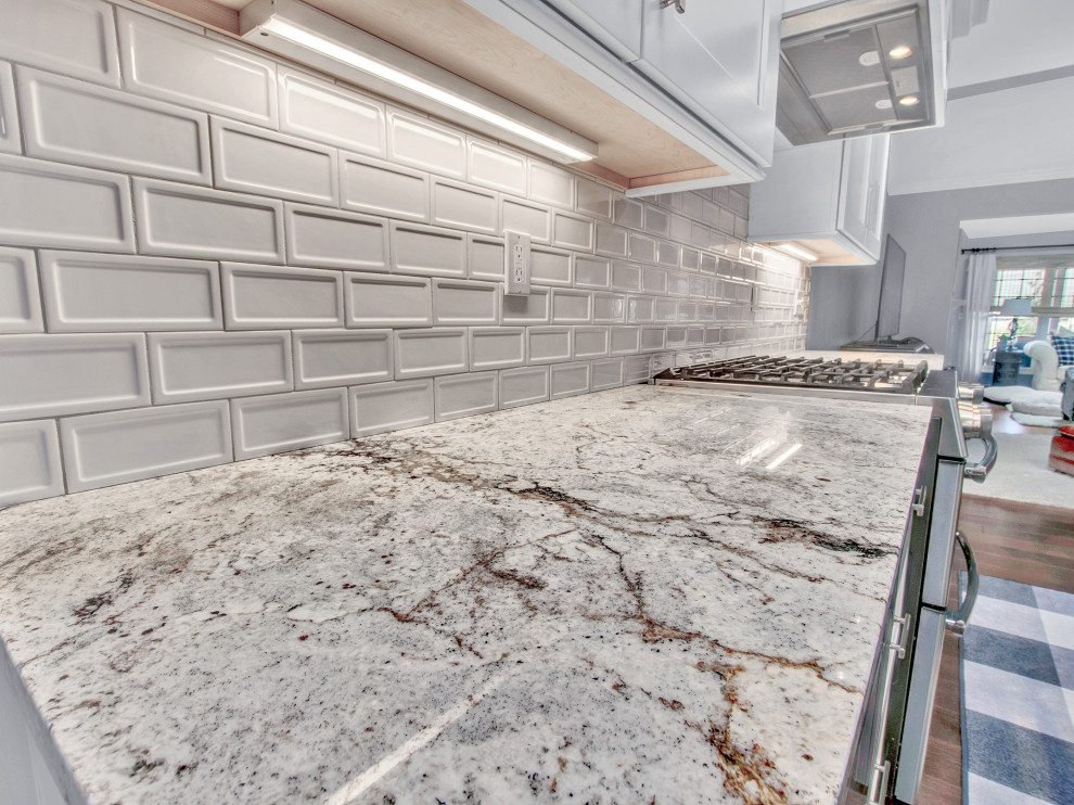 Mid-sized transitional medium tone wood floor, brown floor and vaulted ceiling eat-in kitchen photo in St Louis with an undermount sink, shaker cabinets, white cabinets, granite countertops, white backsplash, subway tile backsplash, stainless steel appliances, an island and multicolored countertops
