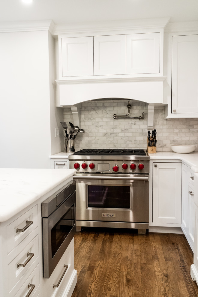This is an example of a small transitional u-shaped kitchen in New York with a farmhouse sink, recessed-panel cabinets, white cabinets, quartzite benchtops, grey splashback, marble splashback, panelled appliances, dark hardwood floors, with island, brown floor and white benchtop.