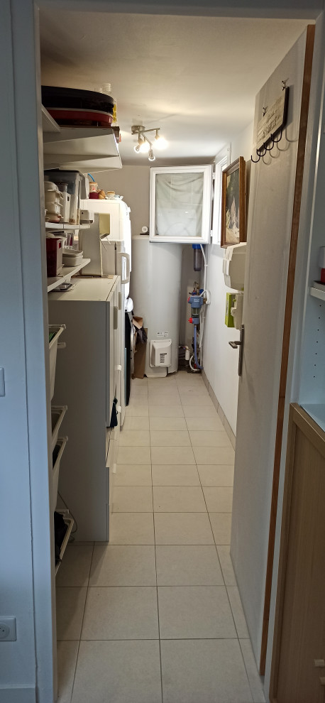 Photo of a mid-sized traditional single-wall utility room in Bordeaux with white walls, ceramic floors, a stacked washer and dryer and beige floor.
