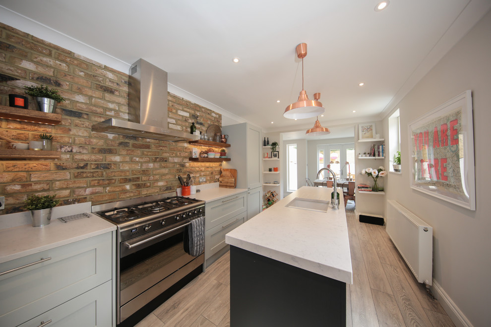 Design ideas for a transitional galley separate kitchen in London with an undermount sink, shaker cabinets, grey cabinets, brown splashback, brick splashback, stainless steel appliances, medium hardwood floors, with island, beige floor and grey benchtop.