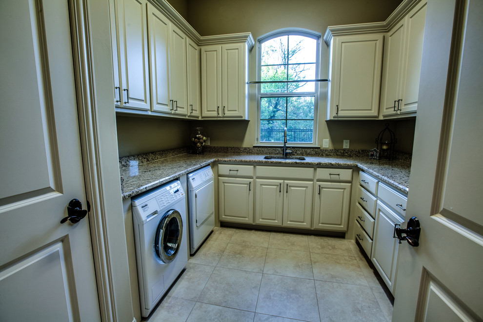Mid-sized traditional u-shaped utility room in Dallas with an undermount sink, raised-panel cabinets, beige cabinets, granite benchtops, beige walls, travertine floors and a side-by-side washer and dryer.