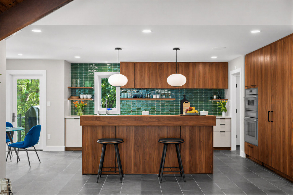 Example of a 1950s l-shaped gray floor kitchen design in DC Metro with flat-panel cabinets, medium tone wood cabinets, green backsplash, stainless steel appliances, an island and white countertops