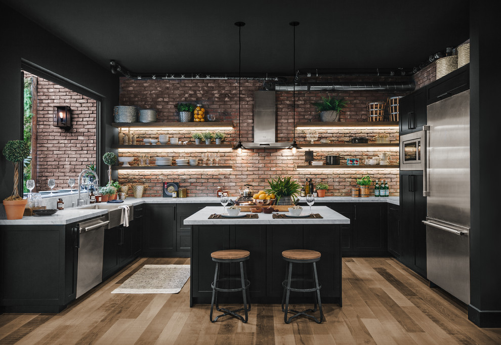 Design ideas for an industrial u-shaped kitchen with a farmhouse sink, shaker cabinets, black cabinets, red splashback, brick splashback, stainless steel appliances, light hardwood floors, with island and white benchtop.