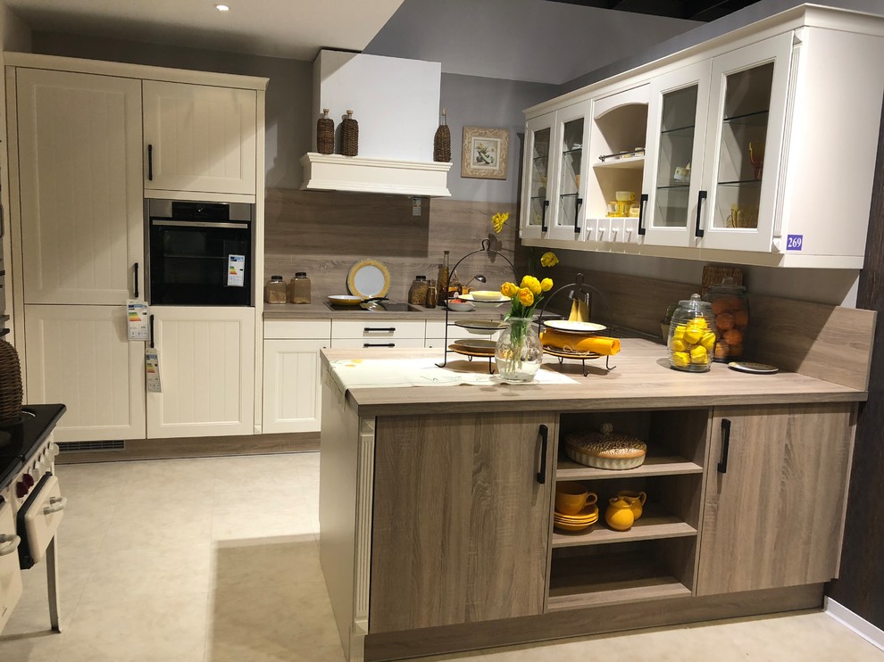 This is an example of a mid-sized tropical u-shaped open plan kitchen in Other with a drop-in sink, raised-panel cabinets, beige cabinets, laminate benchtops, brown splashback, timber splashback, stainless steel appliances, vinyl floors, a peninsula, beige floor and brown benchtop.