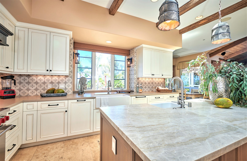 Mid-sized mountain style galley travertine floor, beige floor and exposed beam open concept kitchen photo in Denver with a farmhouse sink, recessed-panel cabinets, white cabinets, quartz countertops, multicolored backsplash, stone tile backsplash, stainless steel appliances, an island and brown countertops