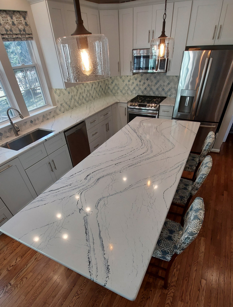 Bild på ett stort funkis vit vitt kök, med en undermonterad diskho, skåp i shakerstil, vita skåp, bänkskiva i kvarts, flerfärgad stänkskydd, stänkskydd i stenkakel, rostfria vitvaror, mellanmörkt trägolv, en köksö och brunt golv