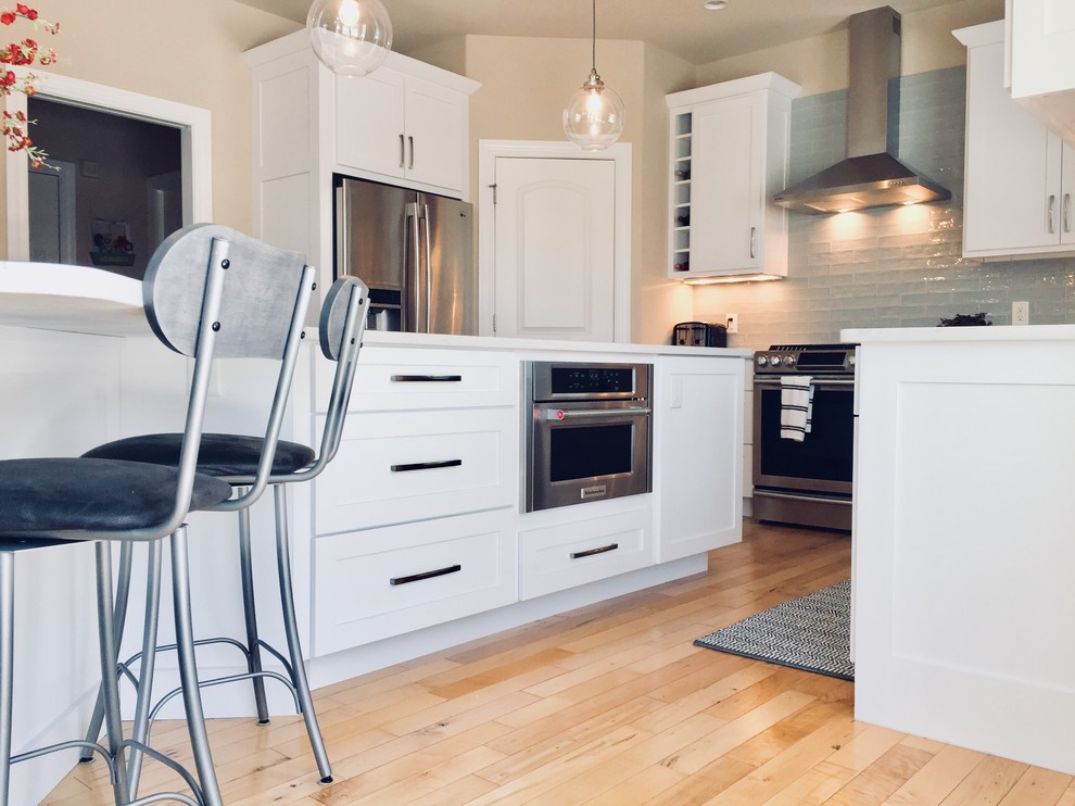 Kitchen - mid-sized transitional light wood floor kitchen idea with an undermount sink, shaker cabinets, white cabinets, quartz countertops, blue backsplash, glass tile backsplash, stainless steel appliances and an island