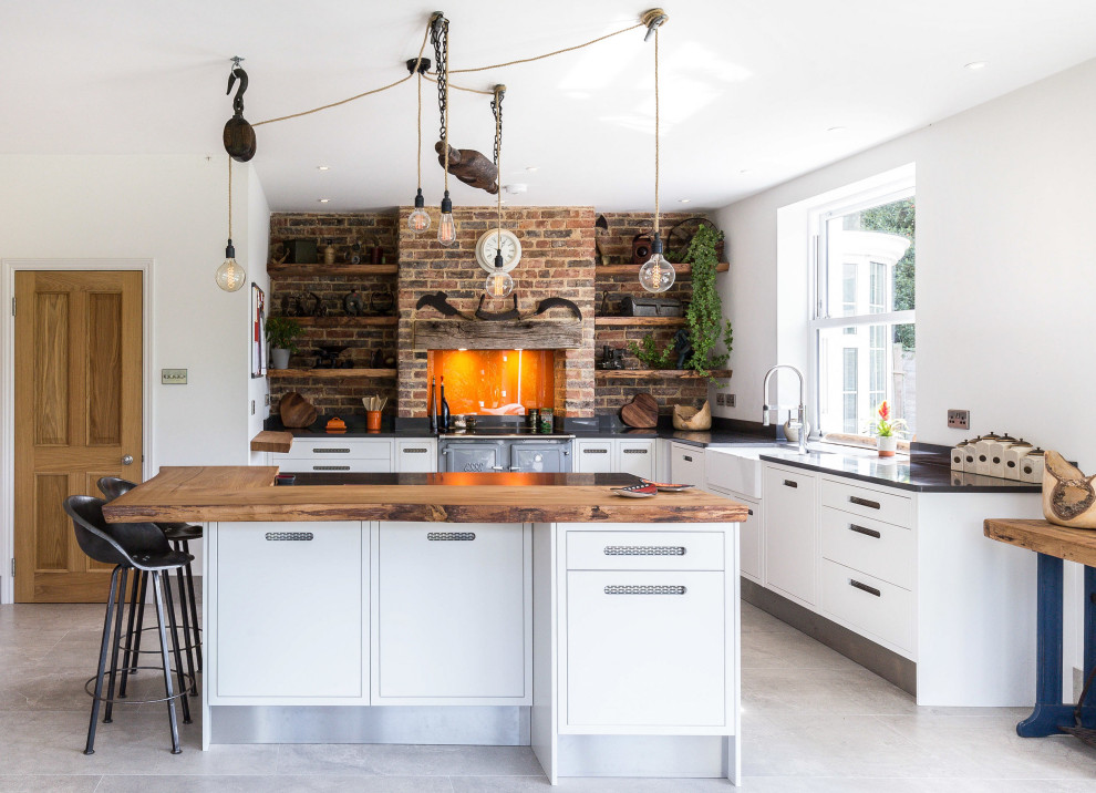 Inspiration for a rural l-shaped kitchen in Sussex with a belfast sink, flat-panel cabinets, white cabinets, coloured appliances, an island, grey floors and black worktops.