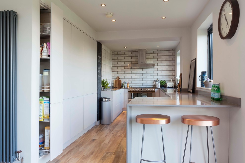 This is an example of a mid-sized eclectic kitchen in Essex with flat-panel cabinets, white cabinets, white splashback, subway tile splashback, stainless steel appliances and brown floor.
