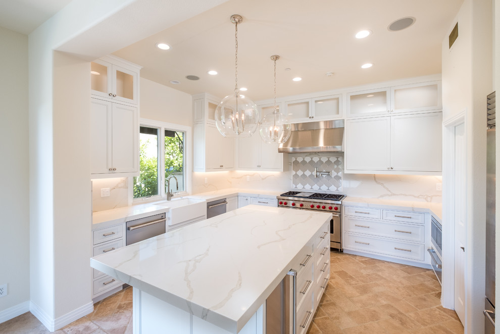 Mid-sized transitional l-shaped porcelain tile and beige floor enclosed kitchen photo in Orange County with a farmhouse sink, recessed-panel cabinets, white cabinets, quartz countertops, white backsplash, marble backsplash, stainless steel appliances and an island