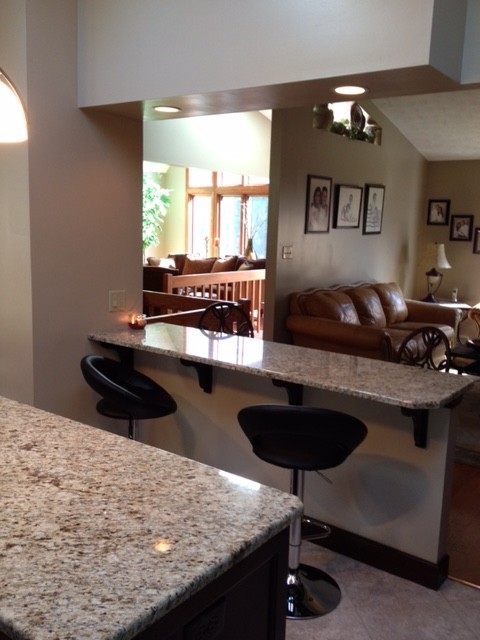 Transitional porcelain tile eat-in kitchen photo with a double-bowl sink, recessed-panel cabinets, brown cabinets, granite countertops, beige backsplash, stone slab backsplash, stainless steel appliances and an island