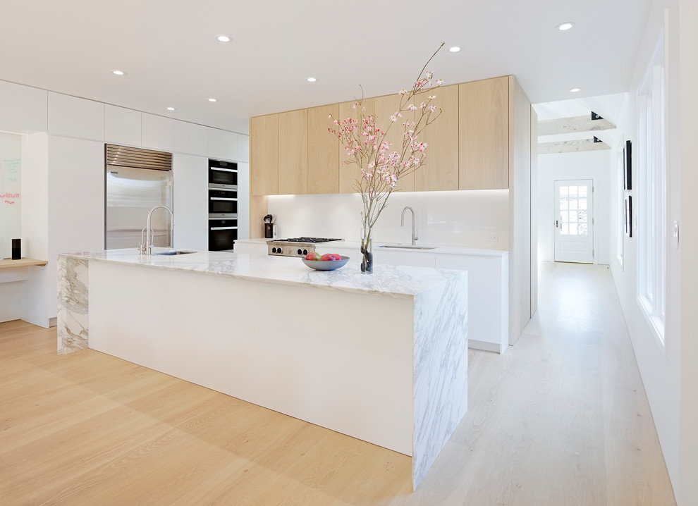 Photo of a mid-sized modern l-shaped open plan kitchen in San Francisco with an undermount sink, flat-panel cabinets, light wood cabinets, marble benchtops, white splashback, stainless steel appliances, light hardwood floors, with island, beige floor, glass sheet splashback and grey benchtop.