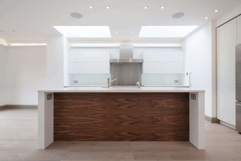 This is an example of a small contemporary l-shaped open plan kitchen in London with an undermount sink, flat-panel cabinets, white cabinets, quartzite benchtops, white splashback, glass tile splashback, stainless steel appliances, light hardwood floors and with island.