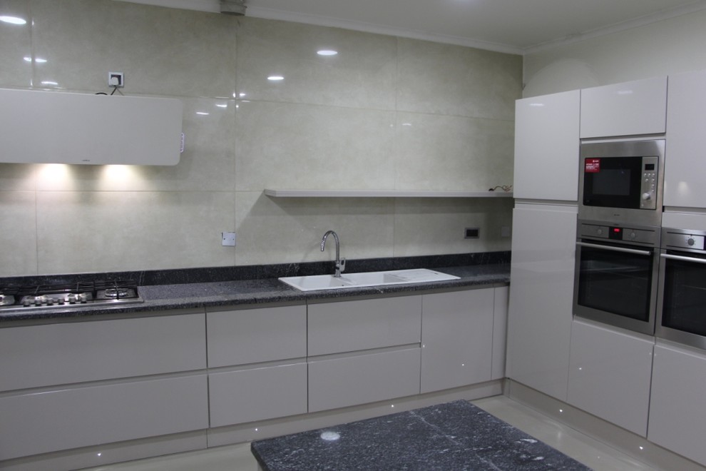 This is an example of an expansive modern u-shaped separate kitchen in Other with a triple-bowl sink, flat-panel cabinets, grey cabinets, granite benchtops, beige splashback, porcelain splashback, stainless steel appliances, ceramic floors, with island, beige floor and black benchtop.