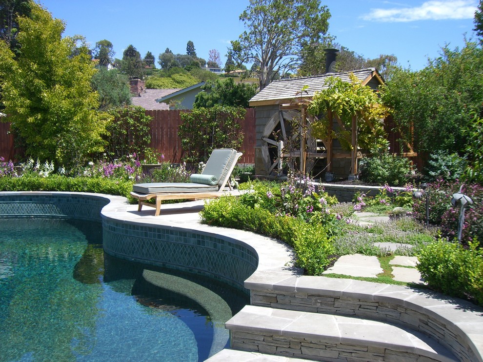 Photo of a large traditional backyard custom-shaped lap pool in Los Angeles with a water feature and natural stone pavers.
