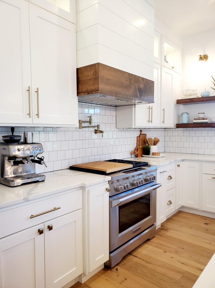 Inspiration for a large country l-shaped open plan kitchen in Portland with a farmhouse sink, shaker cabinets, white cabinets, quartz benchtops, white splashback, ceramic splashback, stainless steel appliances, light hardwood floors, with island, yellow floor and white benchtop.