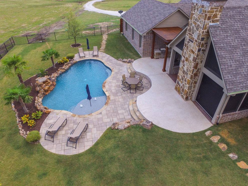 Photo of a mid-sized traditional backyard kidney-shaped pool in Dallas with natural stone pavers.